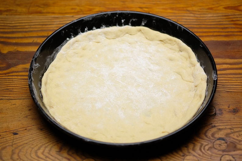 Pizza dough freshly placed in the pizza tray round.