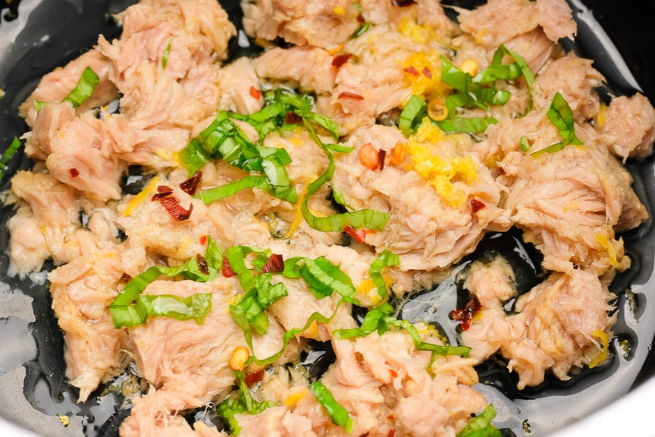 Tuna with oil, basil, lemon juice and lemon zest and chilli in a pan.