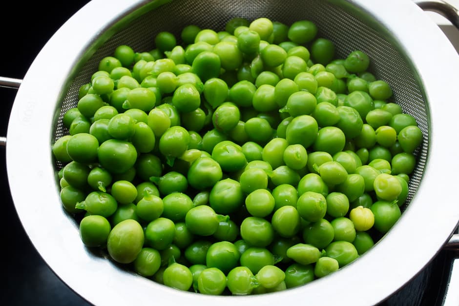 Fresh, cooked, green peas on a kitchen sieve.