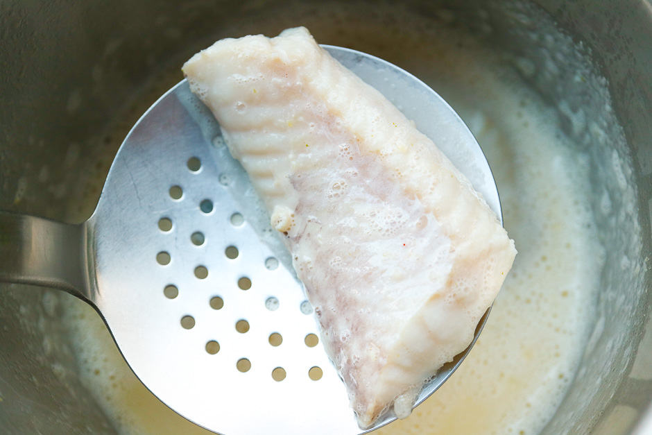 Poached fish over mustard sauce photographed lying on a ladle.