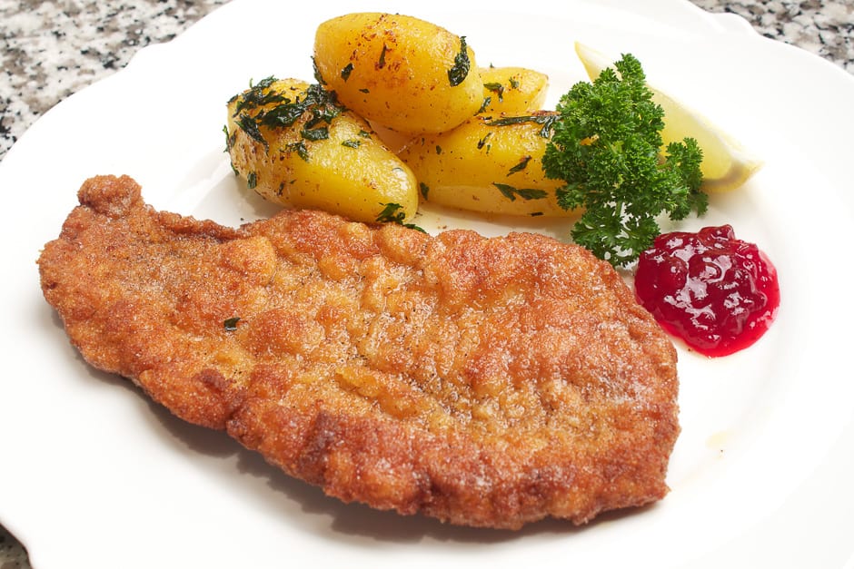 Wiener schnitzel on the plate served with cherries and parsley potatoes.