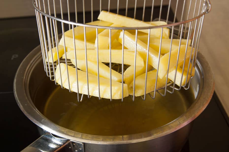 blanched french fries in the frying basket over the hot fat