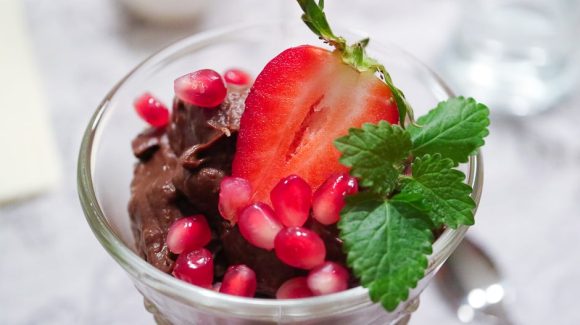 vegan avocado chocolate mousse served as dessert, decorated with strawberries, pomegranate seeds and mint