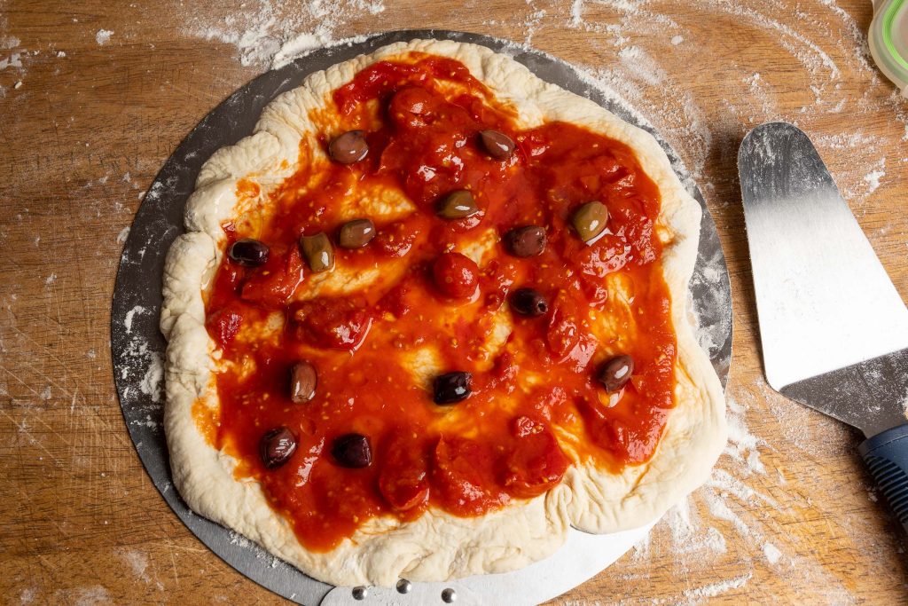 Pizza dough with tomatoes and olives on a pizza peel